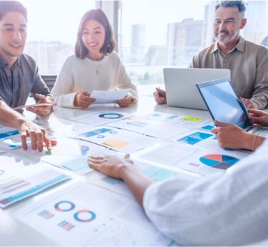 Equipe conversando em uma mesa com diferentes documentos administrativos espalhados.