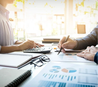 Pessoas na mesa conversando e planejando com papéis na mesa, calculadora e outros documentos.